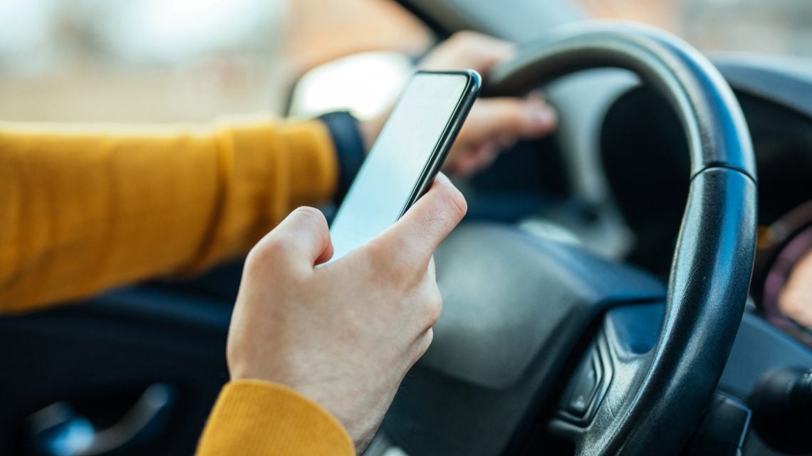 person holding their iphone in their car tracking mileage